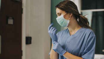 A nurse wearing a face mask and putting on latex gloves