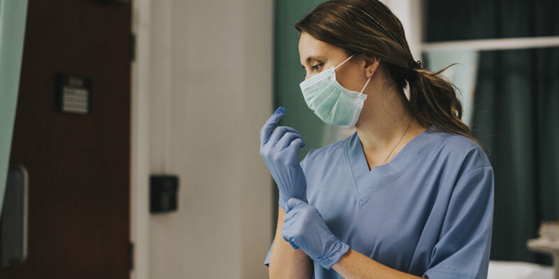 A nurse wearing a face mask and putting on latex gloves