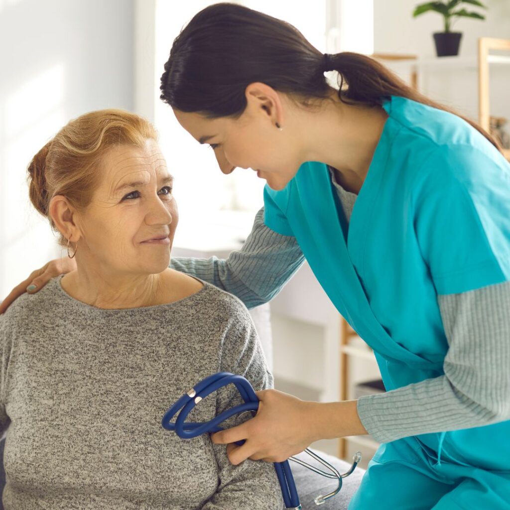 Nurse leaning down and smiling at a woman while holding a stethoscope in her hand.