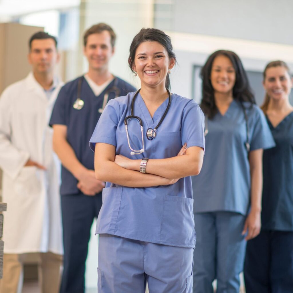 Female nurse standing in the front of multiple other nurses. 